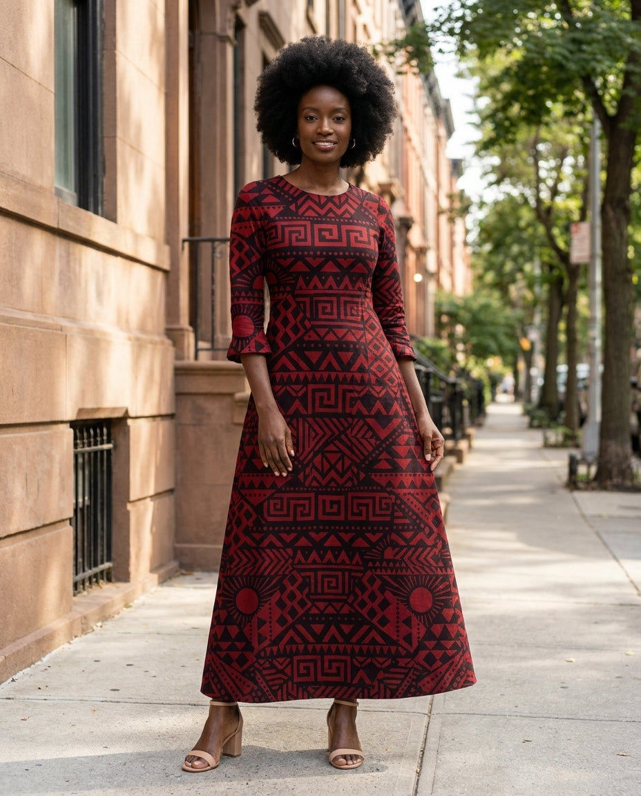 Model with a natural afro wearing the Shaka Long Sleeve Maxi Dress in a deep burgundy-and-black tribal geometric print, ankle-length column silhouette